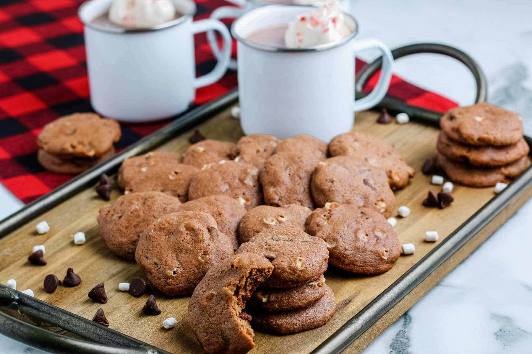 A tray of chocolate chip cookies with marshmallows and two mugs of hot chocolate.