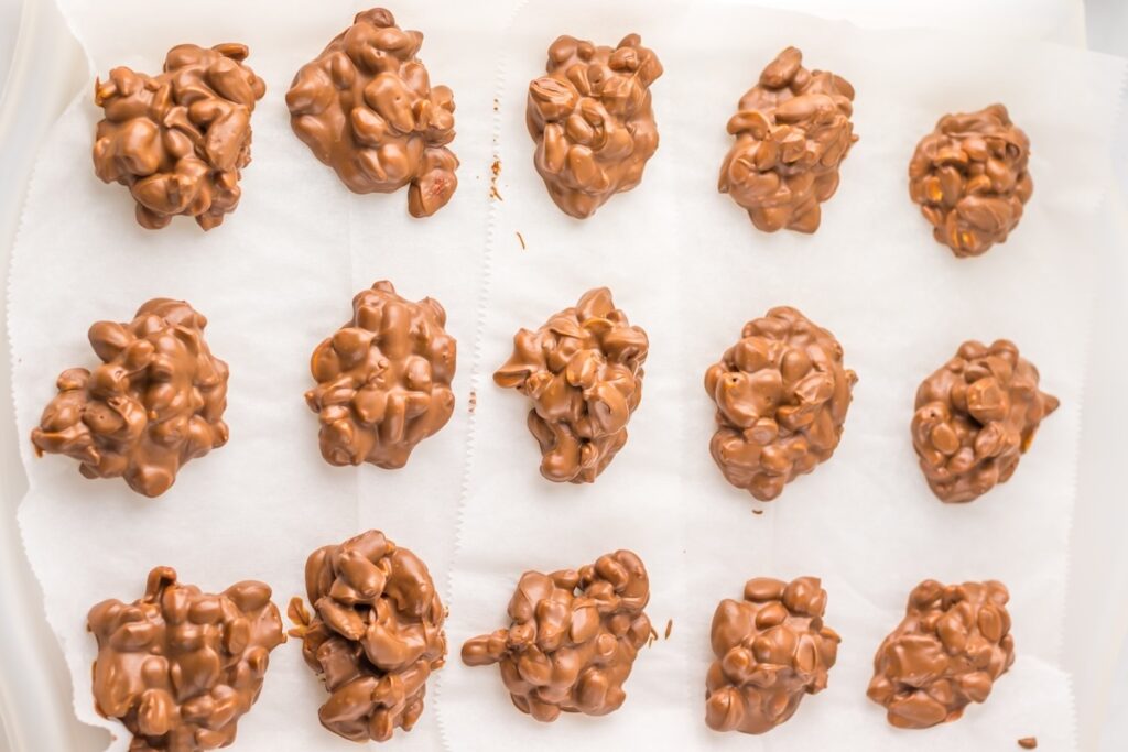 Fourteen clusters of chocolate-covered nuts rest on parchment paper, their textures beautifully contrasting against the pristine background.