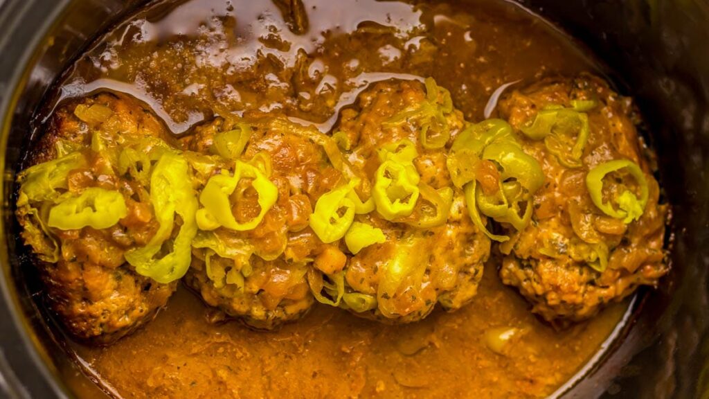 Four meatballs in a rich sauce, topped with sliced green peppers.