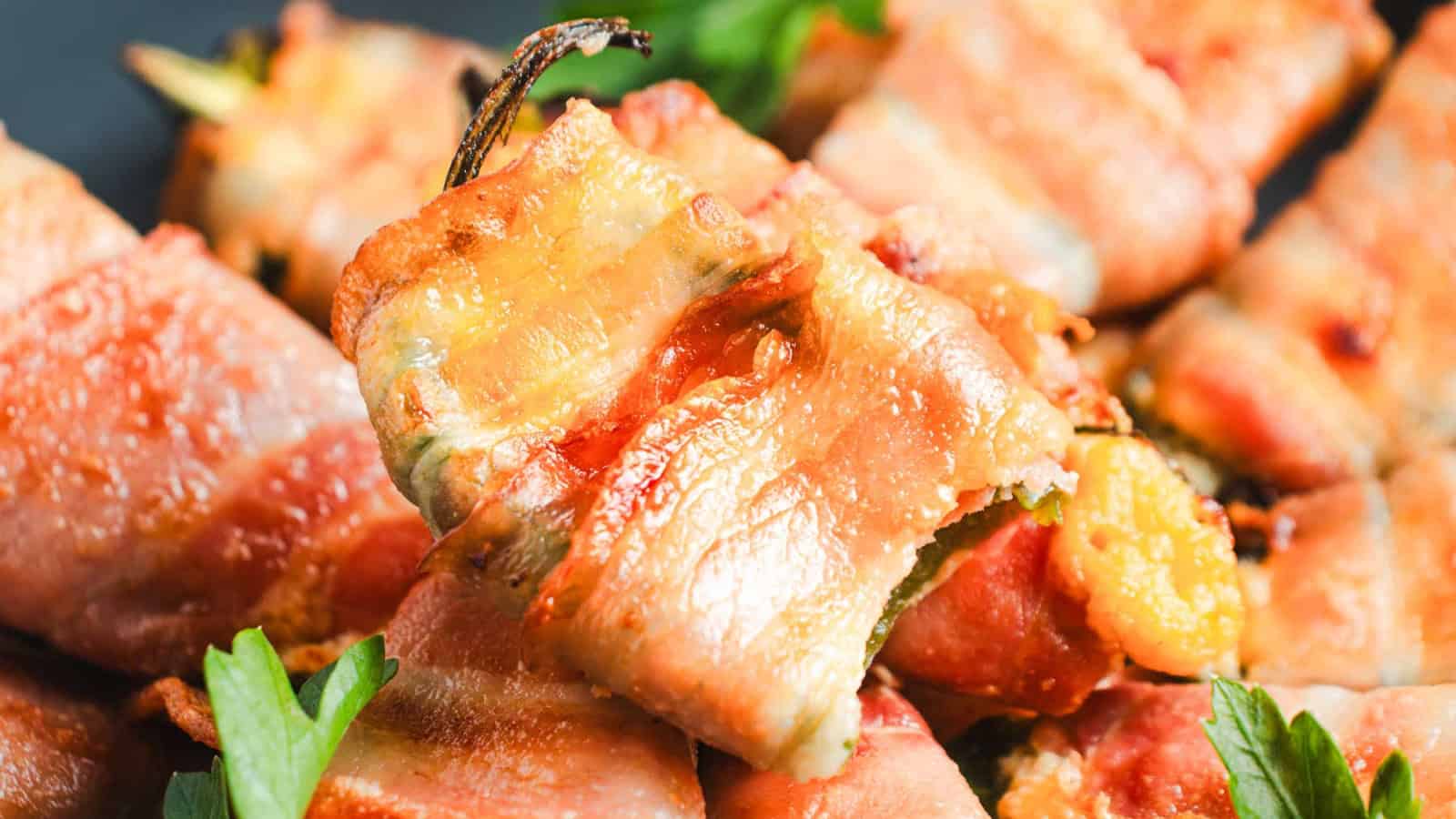 Plate of bacon-wrapped peppers filled with cheese, garnished with parsley, next to a grated cheese block and grater on a wooden board.