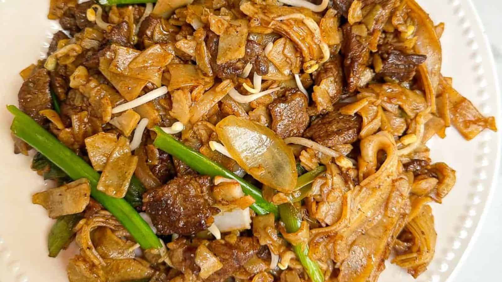 A plate of stir-fried noodles with beef, green beans, bean sprouts, and onions.