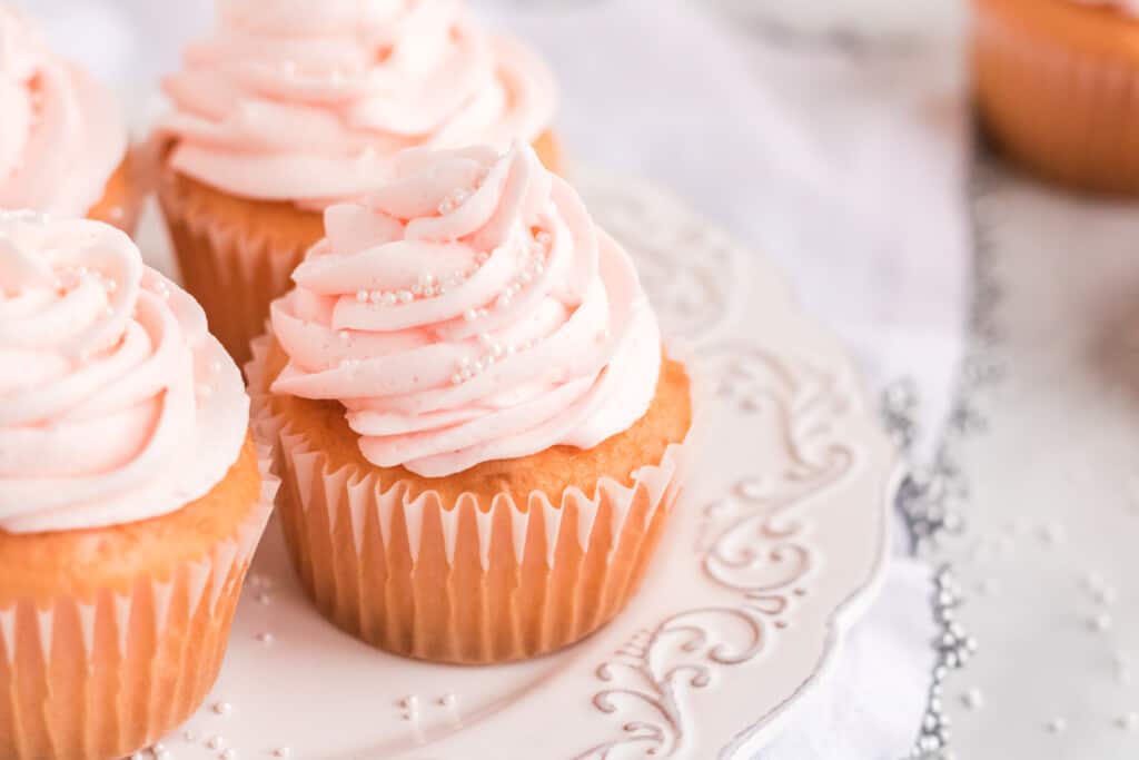Pink frosted cupcakes with white sprinkles on a decorative white plate.