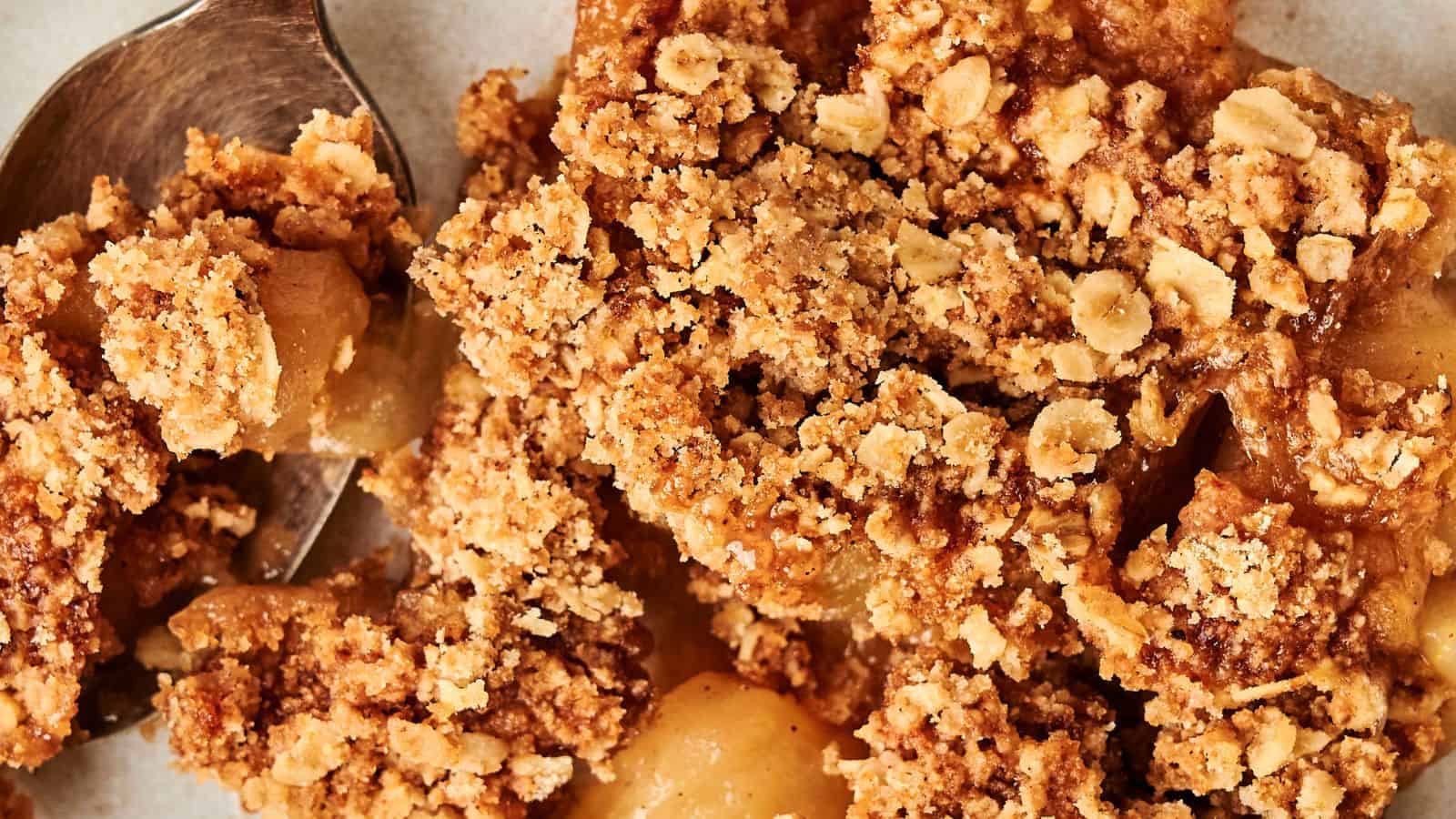 Close-up of apple crumble with oats and brown sugar topping. A spoon is partially visible on the left.