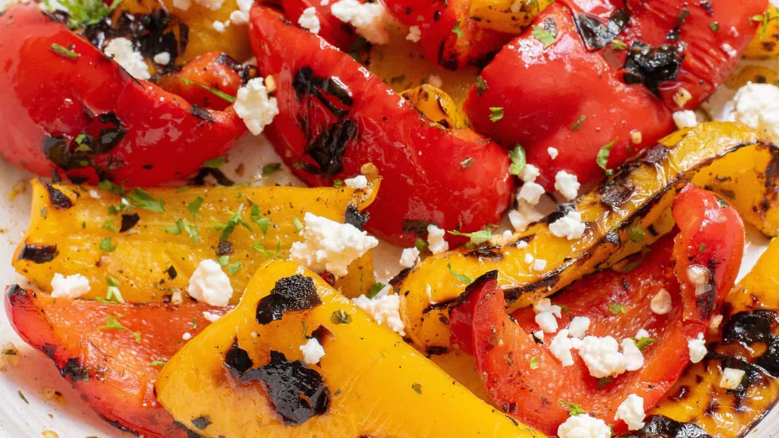 Grilled red and yellow bell peppers with char marks, topped with crumbled feta cheese and garnished with herbs.