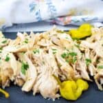 Low-Carb Mississippi Chicken garnished with parsley is served on a slate platter with yellow peppers.