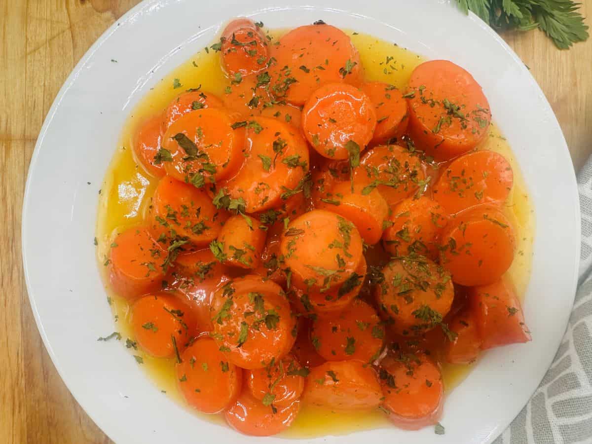 A plate of glazed carrot slices topped with chopped herbs, served with a light sauce.