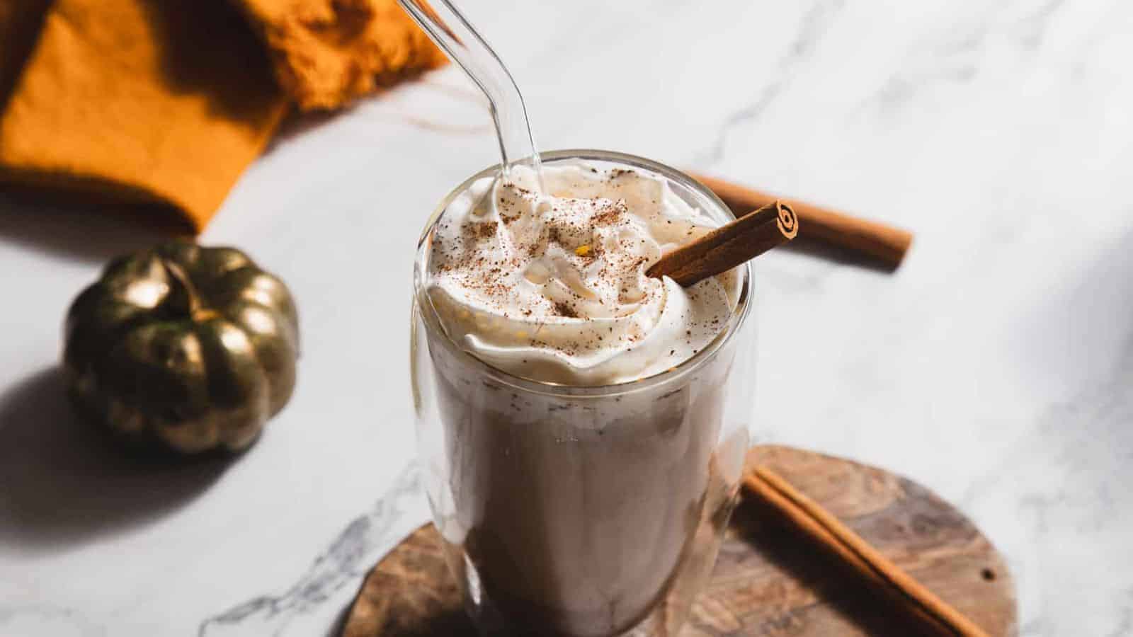 A pumpkin spice cold brew in a glass, topped with whipped cream and a cinnamon stick, with decorative elements in the background.