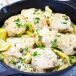 Low-carb skillet Chicken with Lemon, Artichokes & Feta in a black skillet, garnished with lemon wedges and parsley.