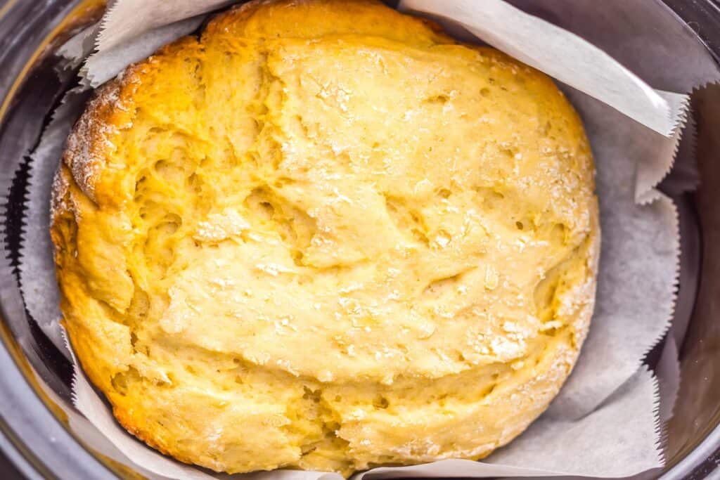 A golden-brown round loaf of bread on parchment paper, in a baking dish.