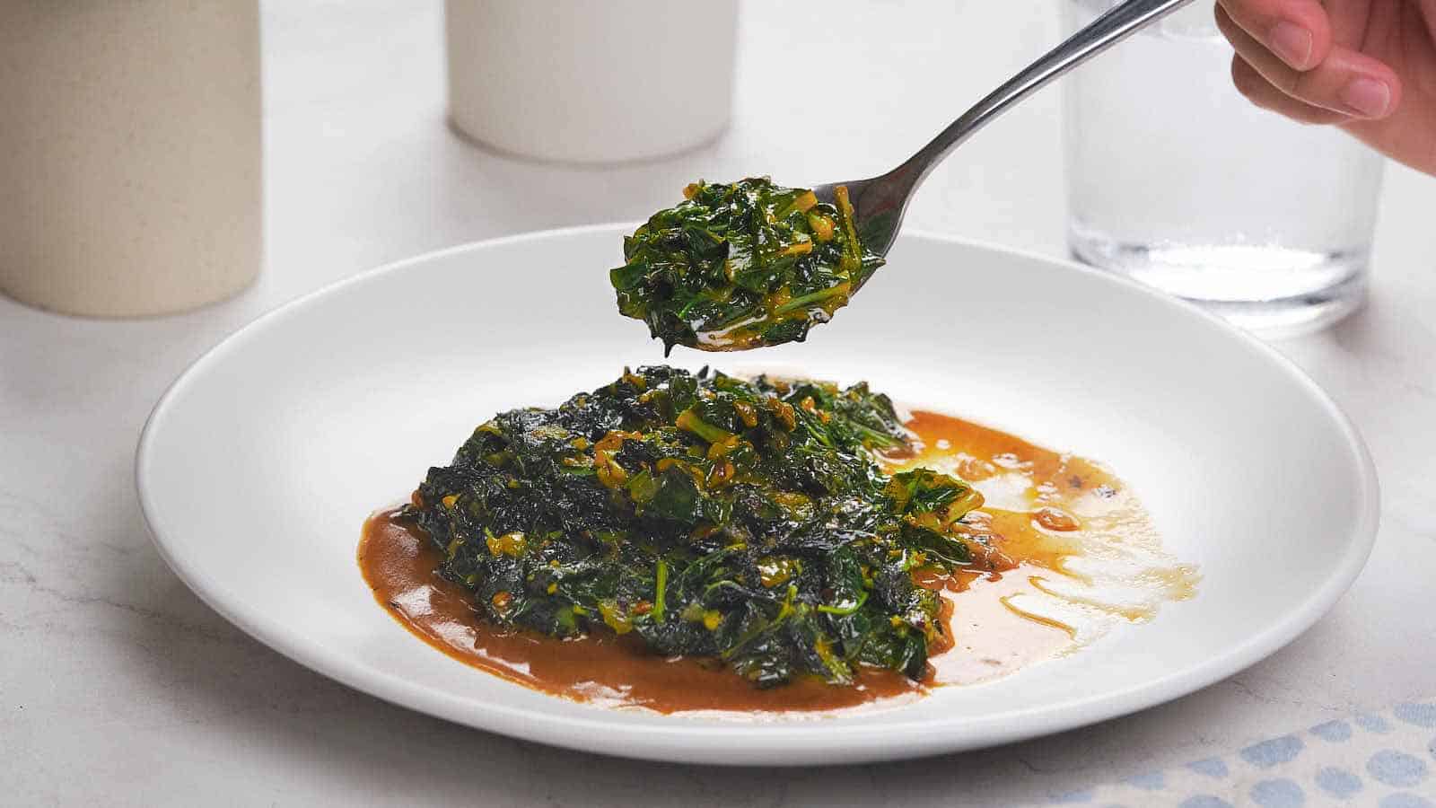 A plate of saut&eacute;ed leafy greens in sauce, with a fork holding a portion above the dish.