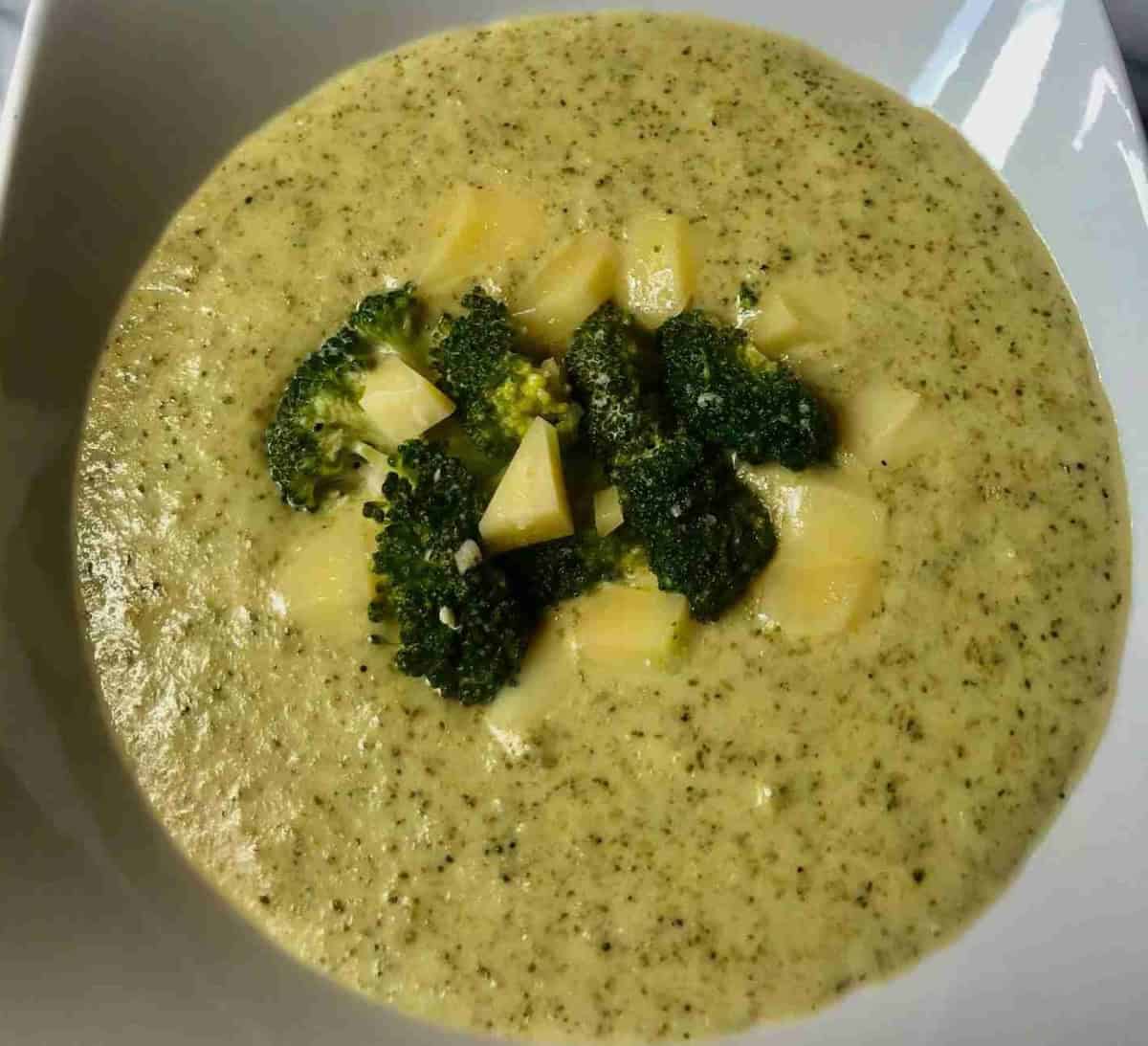 A bowl of broccoli cheese soup garnished with broccoli florets and cheese cubes.