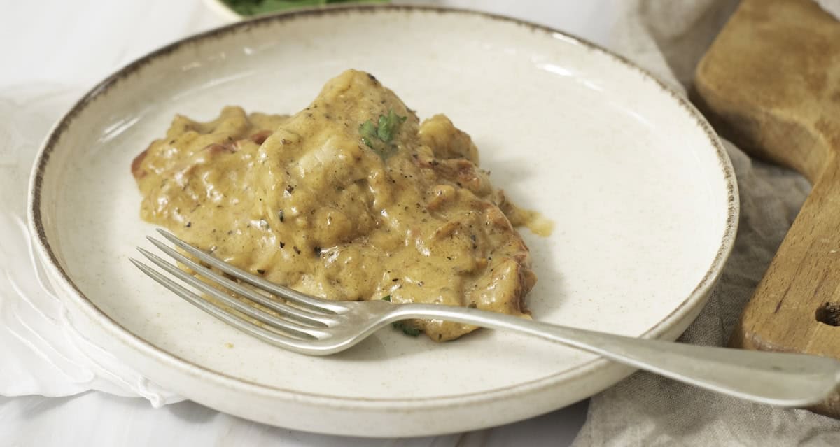 Plate with creamy sauced meat and herbs, accompanied by a fork on the side.