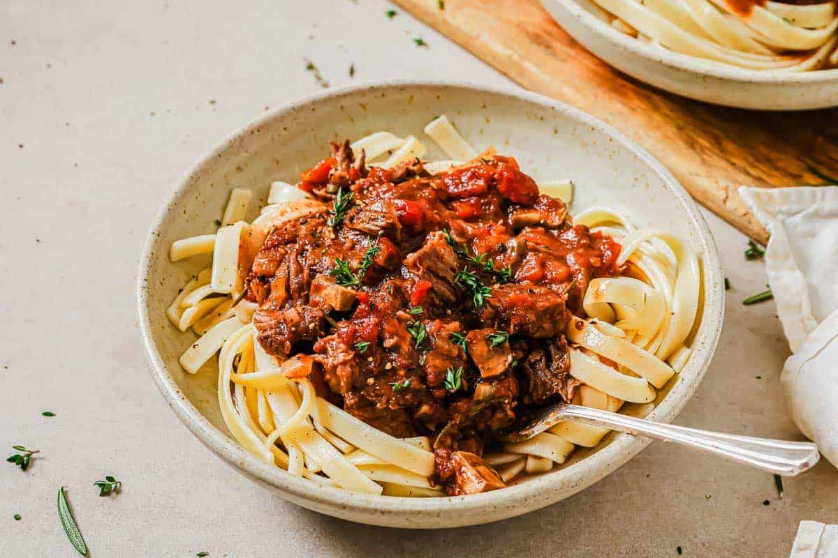 Slow cooker short rib ragu in a bowl over mashed sweet potatoes with a fork.