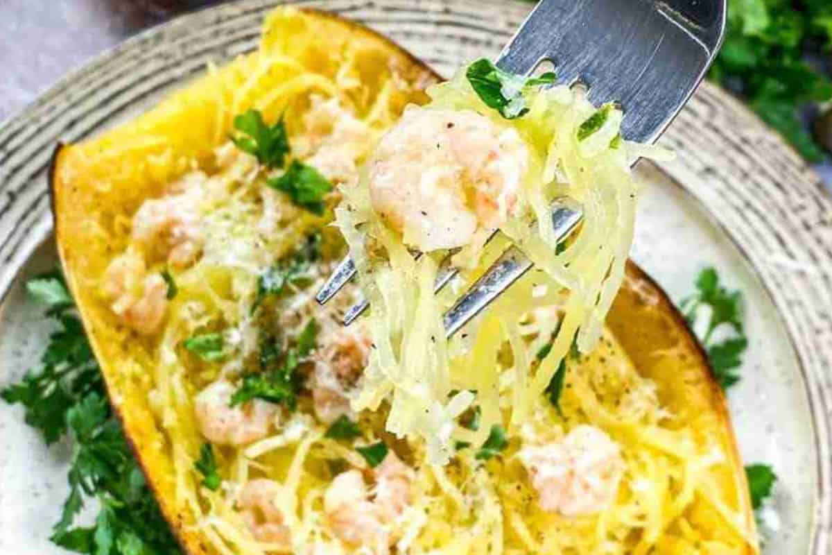 Spaghetti squash with shrimp, garnished with parsley on a plate, with a fork holding a portion.