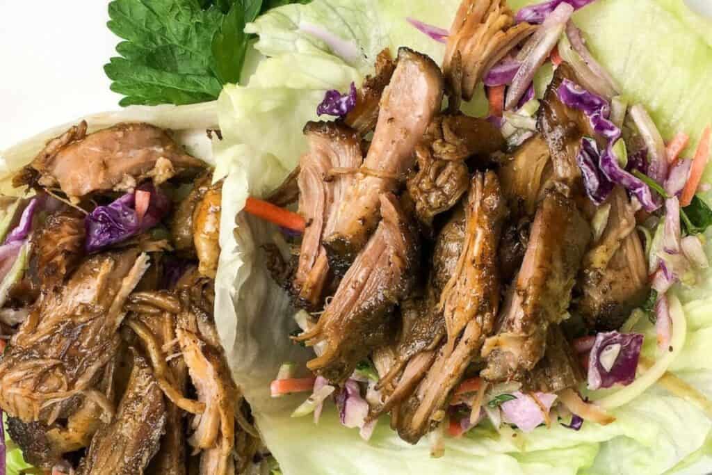 Pulled pork served in lettuce wraps with shredded carrots and purple cabbage.