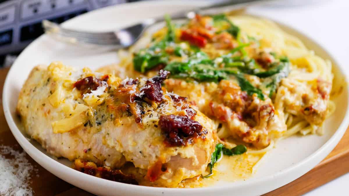Plate with creamy chicken breast topped with herbs, sundried tomatoes, and sauce, served with spinach.