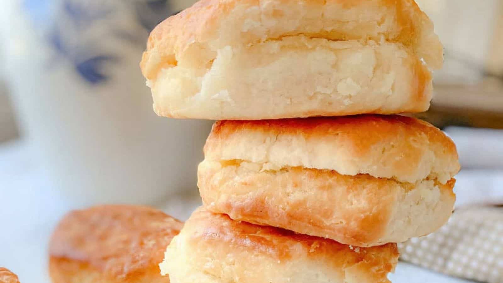 A stack of three golden-brown, flaky biscuits on a white surface, with a blurry background.