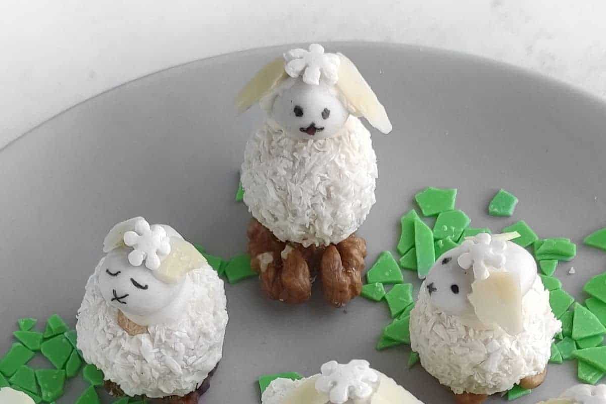 Three Easter Bunny Treats desserts made of coconut-covered balls with walnut feet and white candy decorations are on a gray plate with green candy shards.