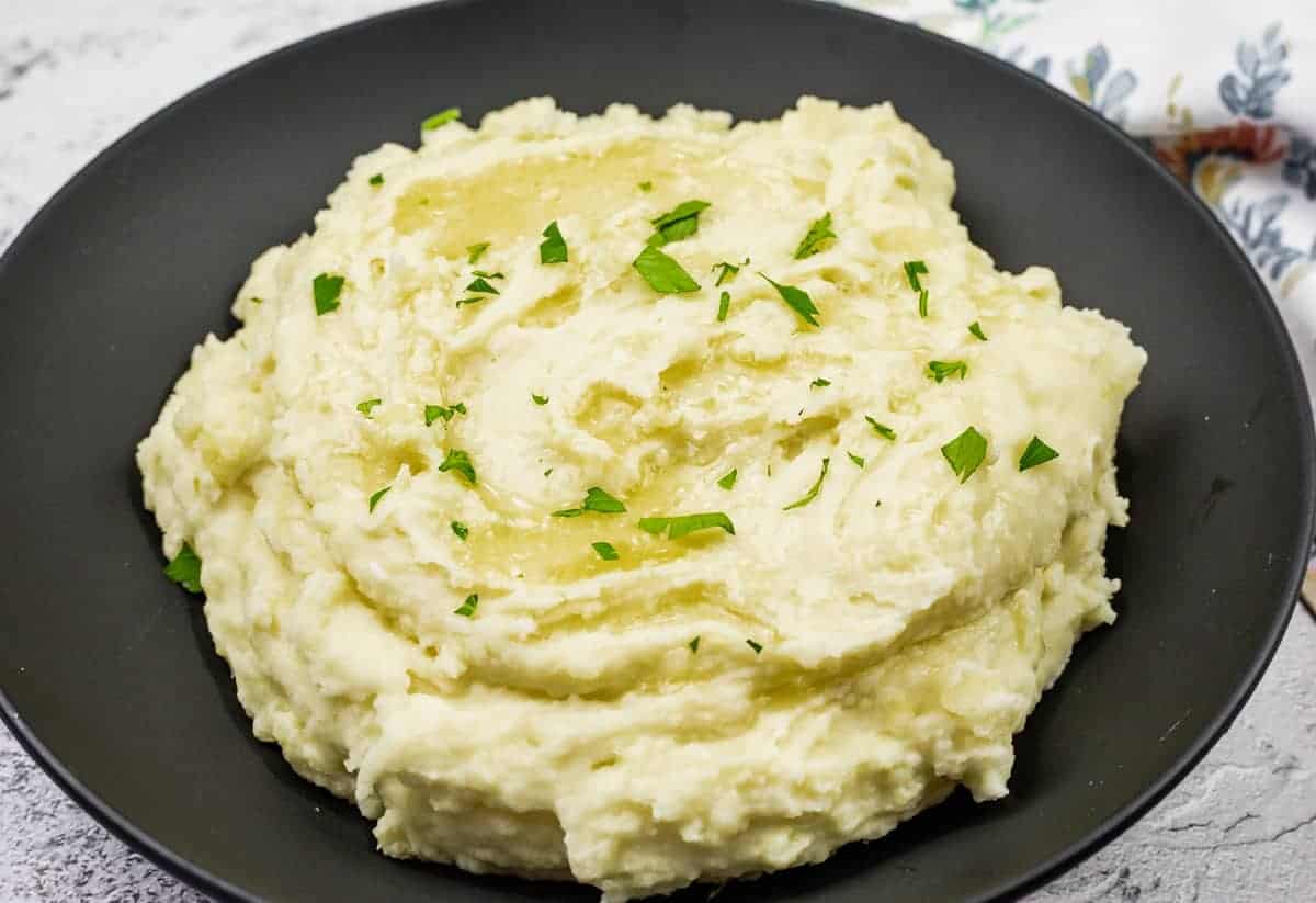 A black bowl filled with Grandma's Mashed Potatoes topped with chopped parsley.