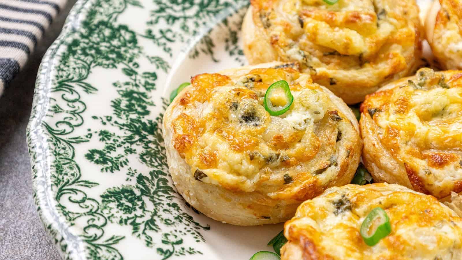 Baked pastry rolls with cheese and herbs on a decorative green and white plate.