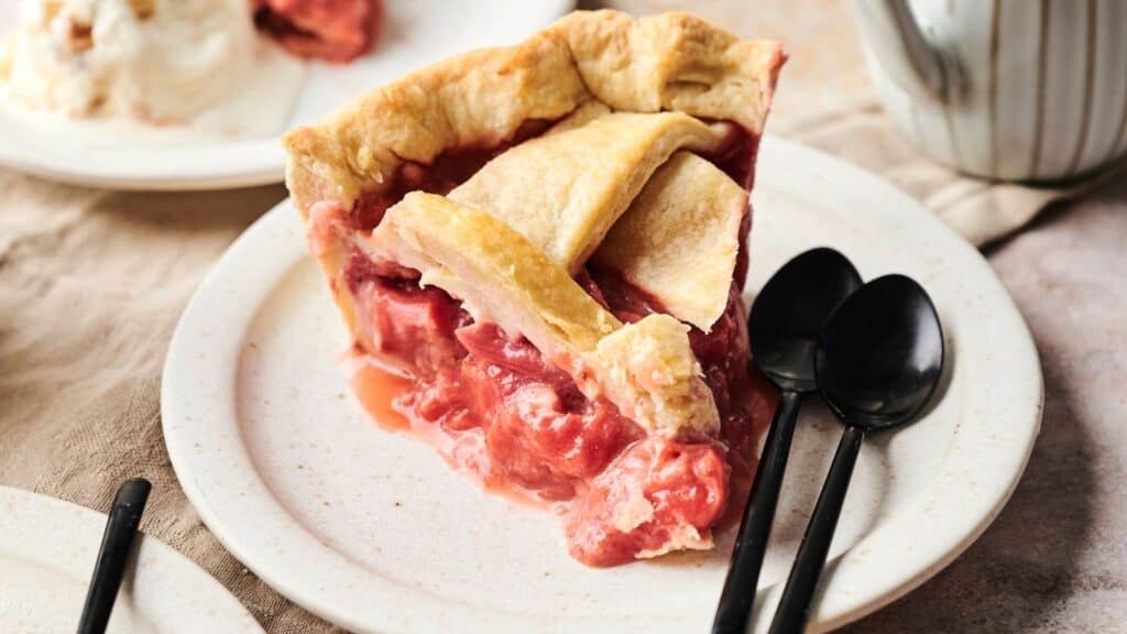Slice of cherry pie on a plate with two black spoons beside it.