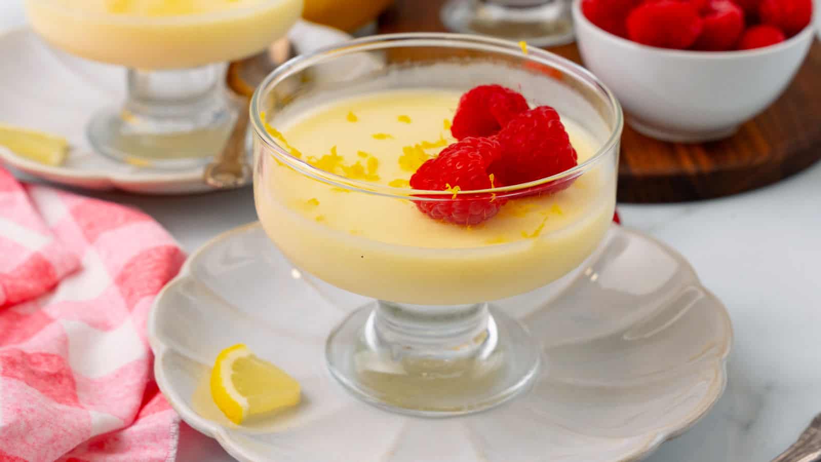 Lemon posset in red ramekins on a yellow and white towel.