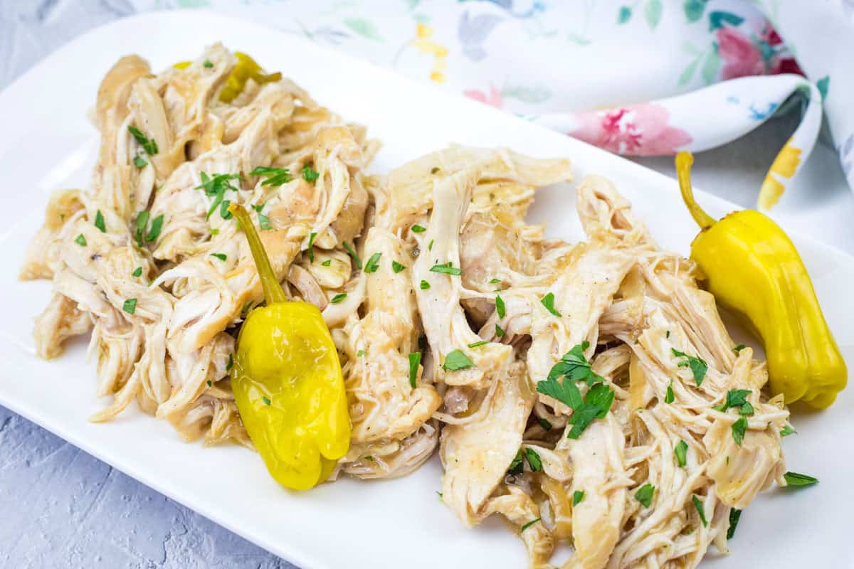 Mississippi Chicken - Slow Cooker with herbs and two yellow peppers on a white rectangular plate.