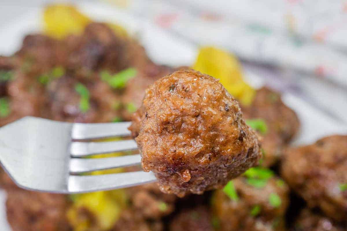 A close-up of a meatball on a fork, with more meatballs in the background.