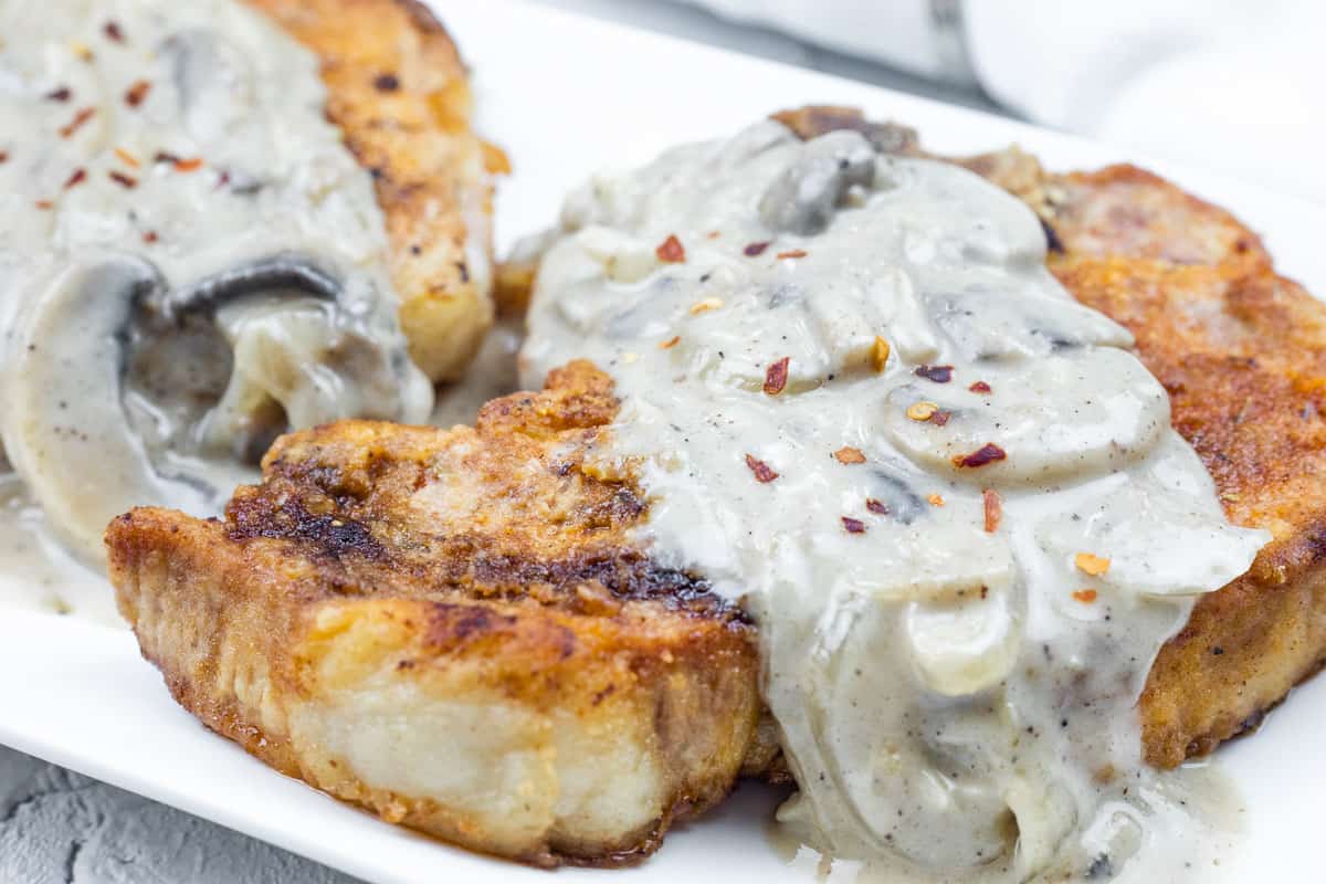 Golden-brown Saucy Smothered Pork Chops topped with a creamy mushroom and onion gravy, garnished with red pepper flakes.