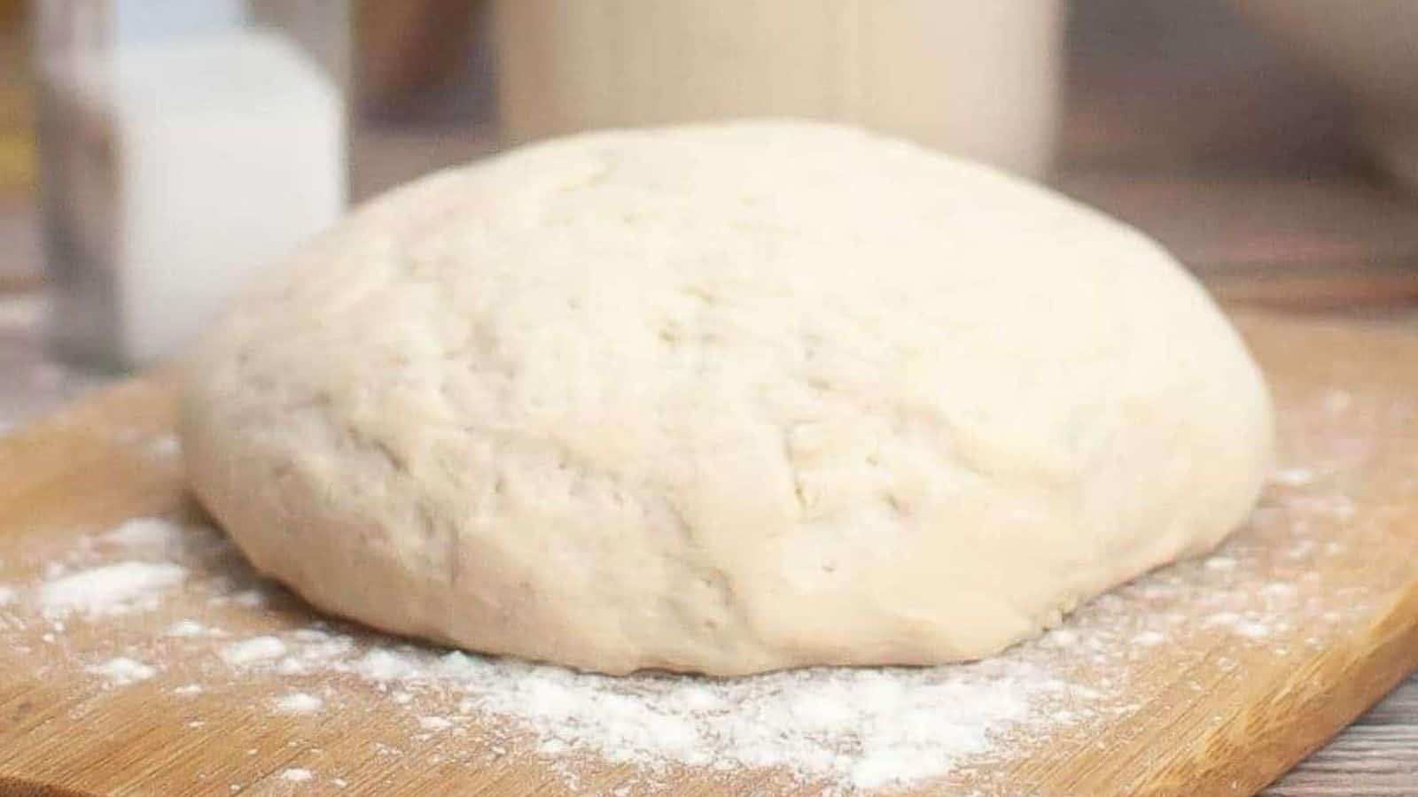 A slice of sourdough pepperoni pizza on a white plate with a ball of dough on a wooden board in the background.