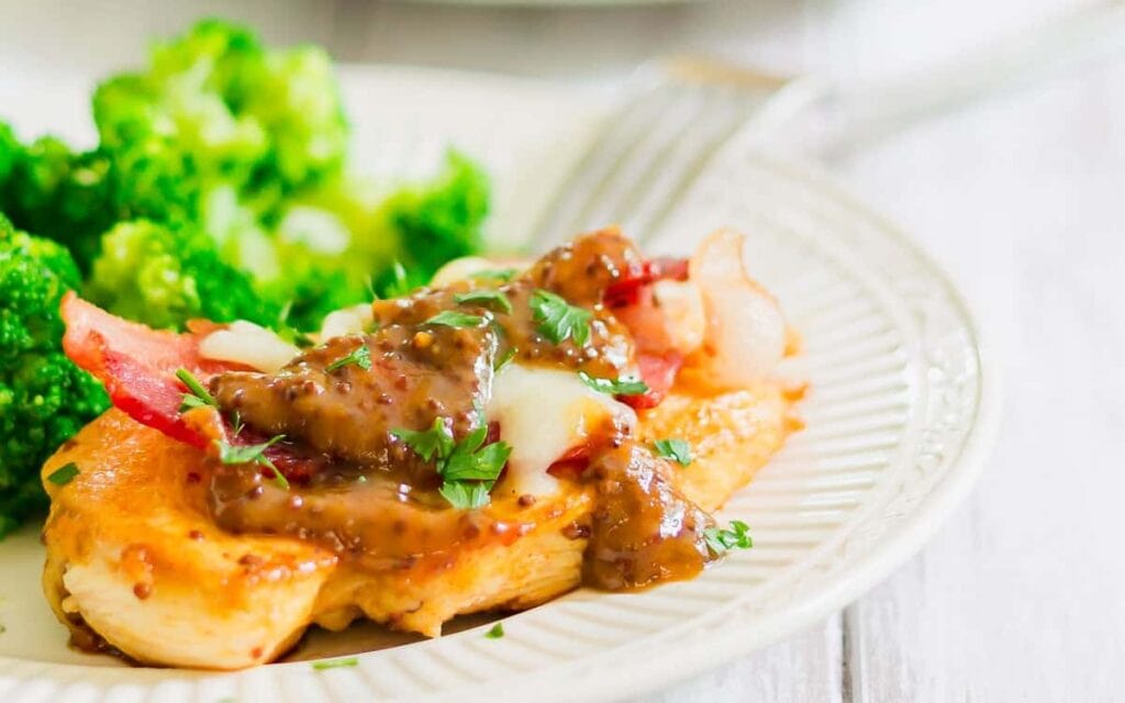 Plate of chicken topped with bacon, cheese, and sauce, garnished with herbs. Broccoli is on the side. A fork is partially visible.
