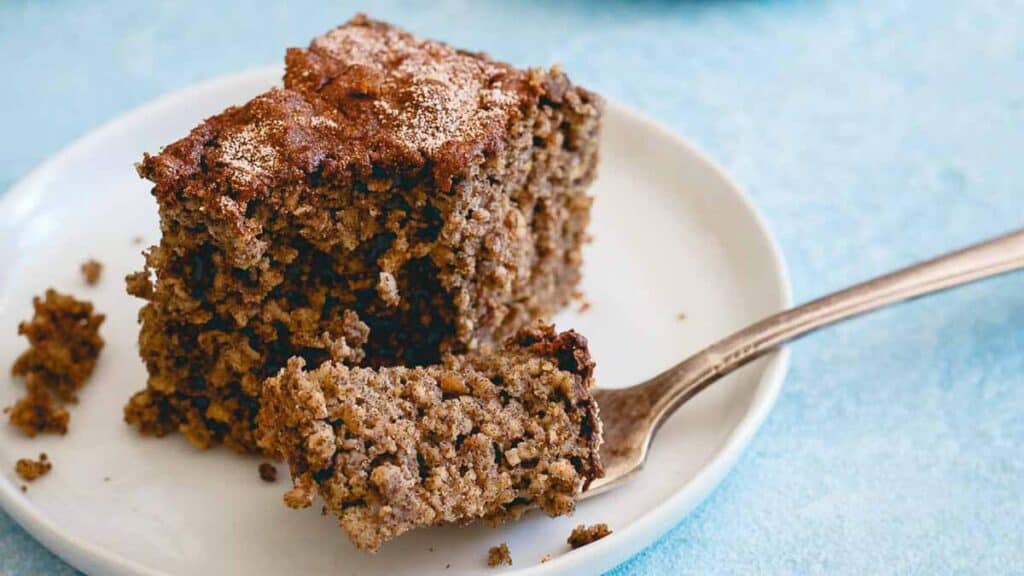A slice of brown, crumbly cake on a white plate with a fork.