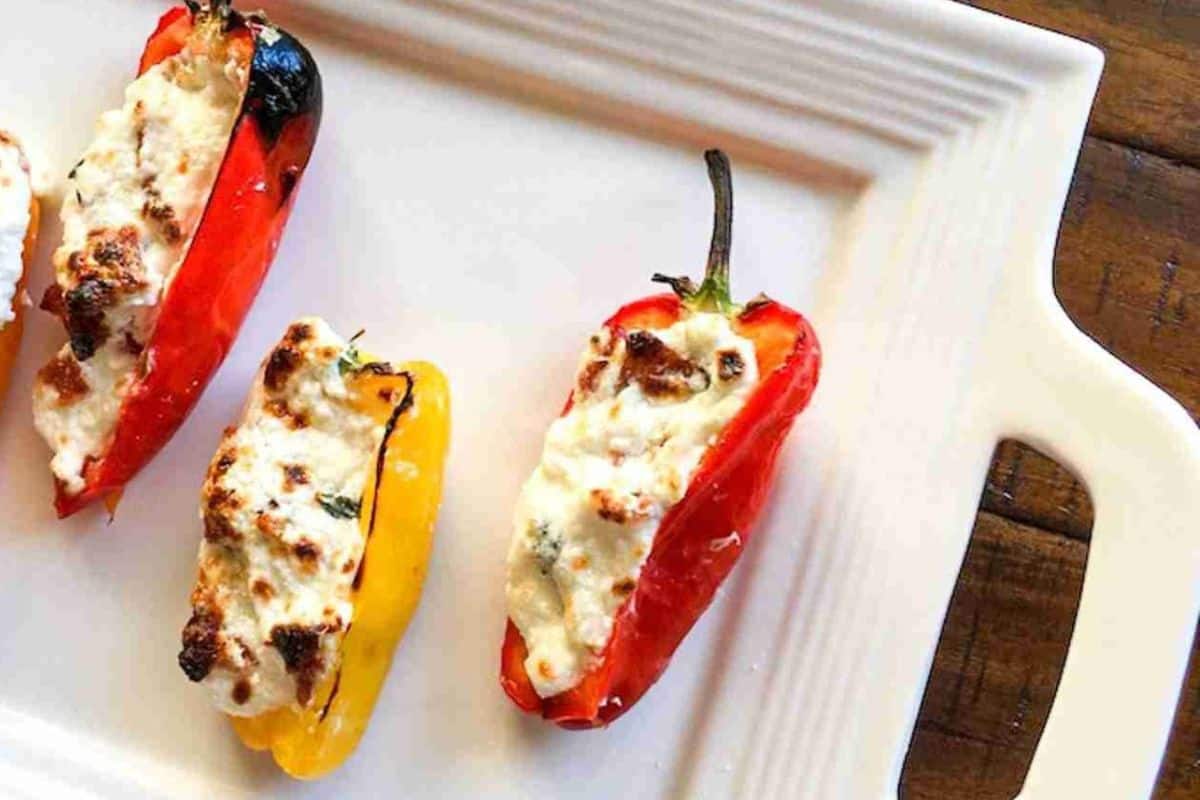 Three stuffed mini bell peppers filled with cheese are arranged on a white rectangular plate.