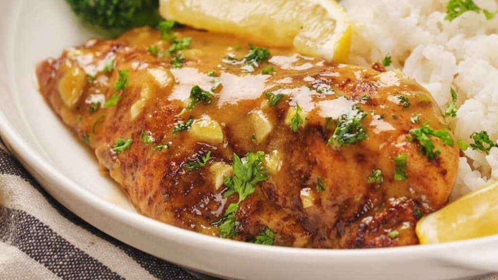 Honey mustard chicken with lemon glaze, garnished with parsley, served alongside white rice.