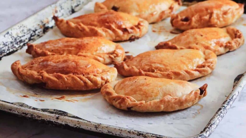 Eight golden-brown pasties on a parchment-lined baking tray.