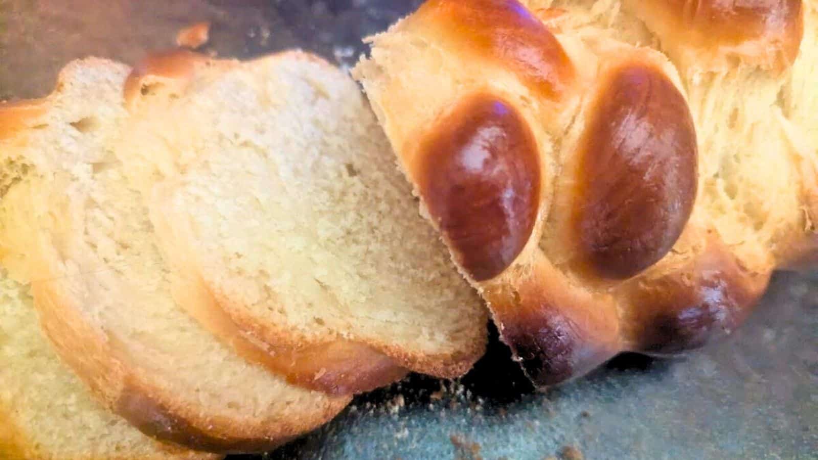 Sliced braided loaf of bread on a dark surface, showing a golden-brown crust and light, soft interior.