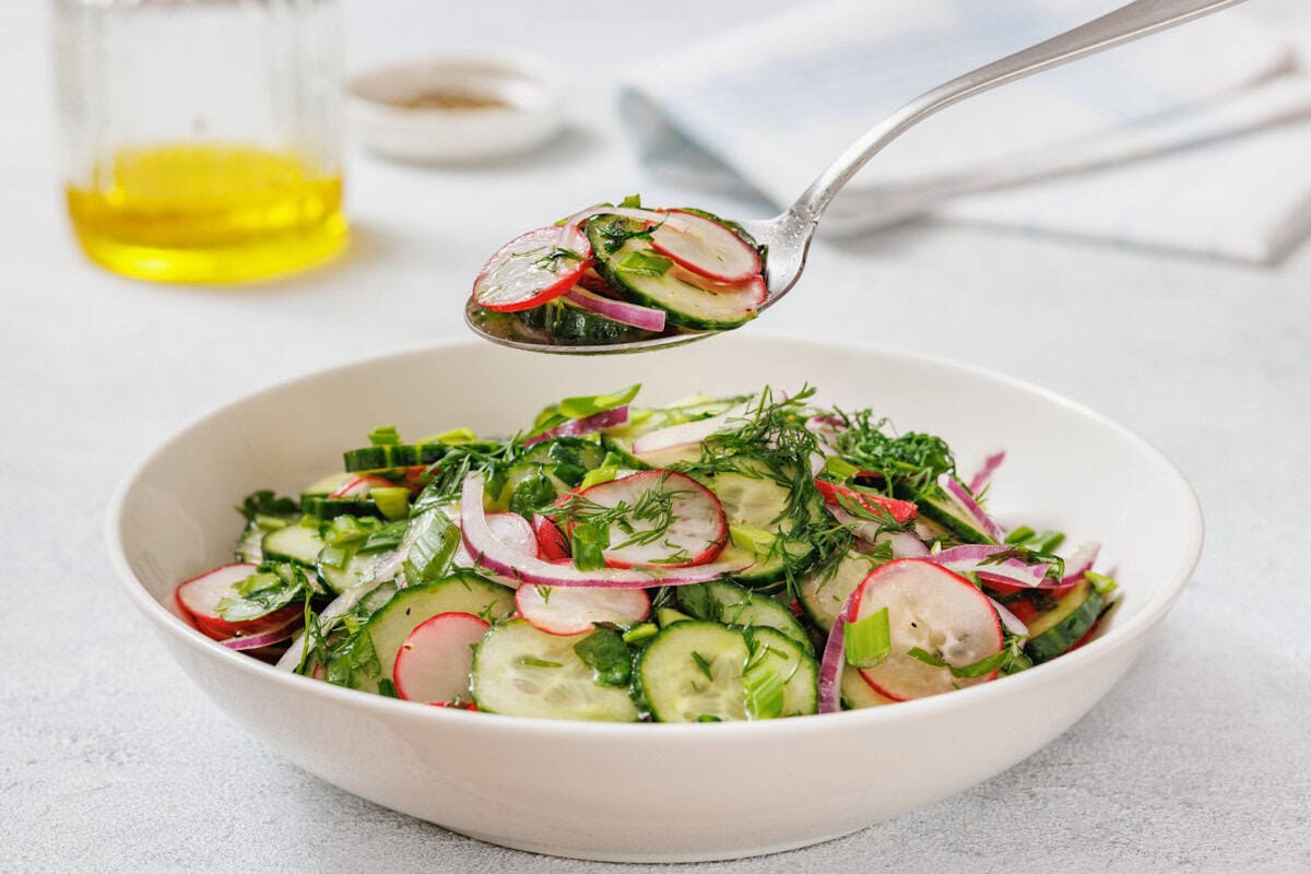 A spoonful of Radish Salad is held above a white bowl filled with the same salad.
