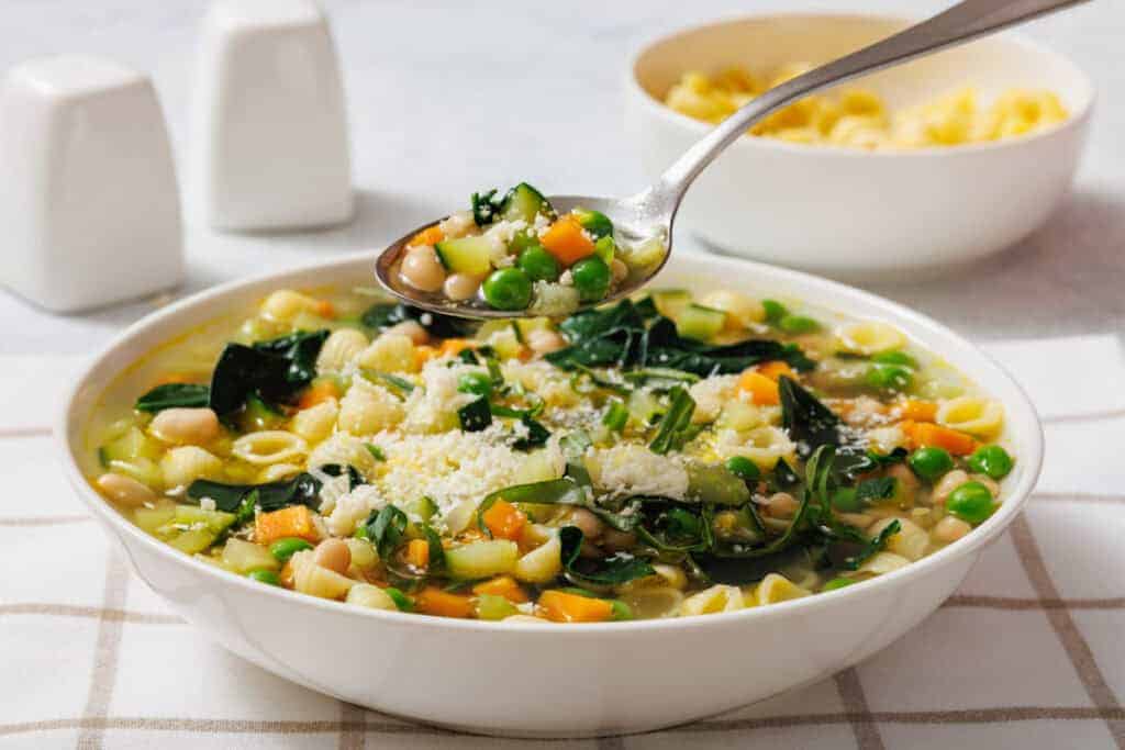 A spoon holds a portion above the bowl of Spring Minestrone.