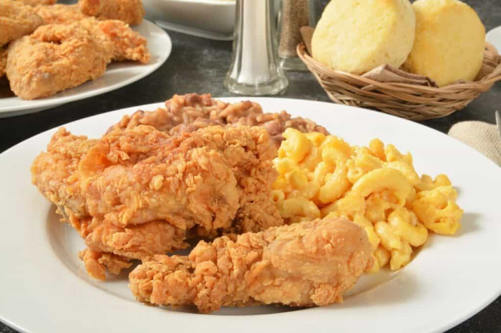 Plate with fried chicken, macaroni and cheese, and baked beans. Basket of biscuits in the background.