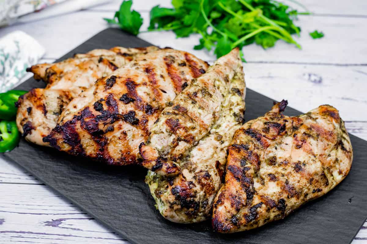 Grilled lime garlic chicken breasts on a black plate, accompanied by cilantro.