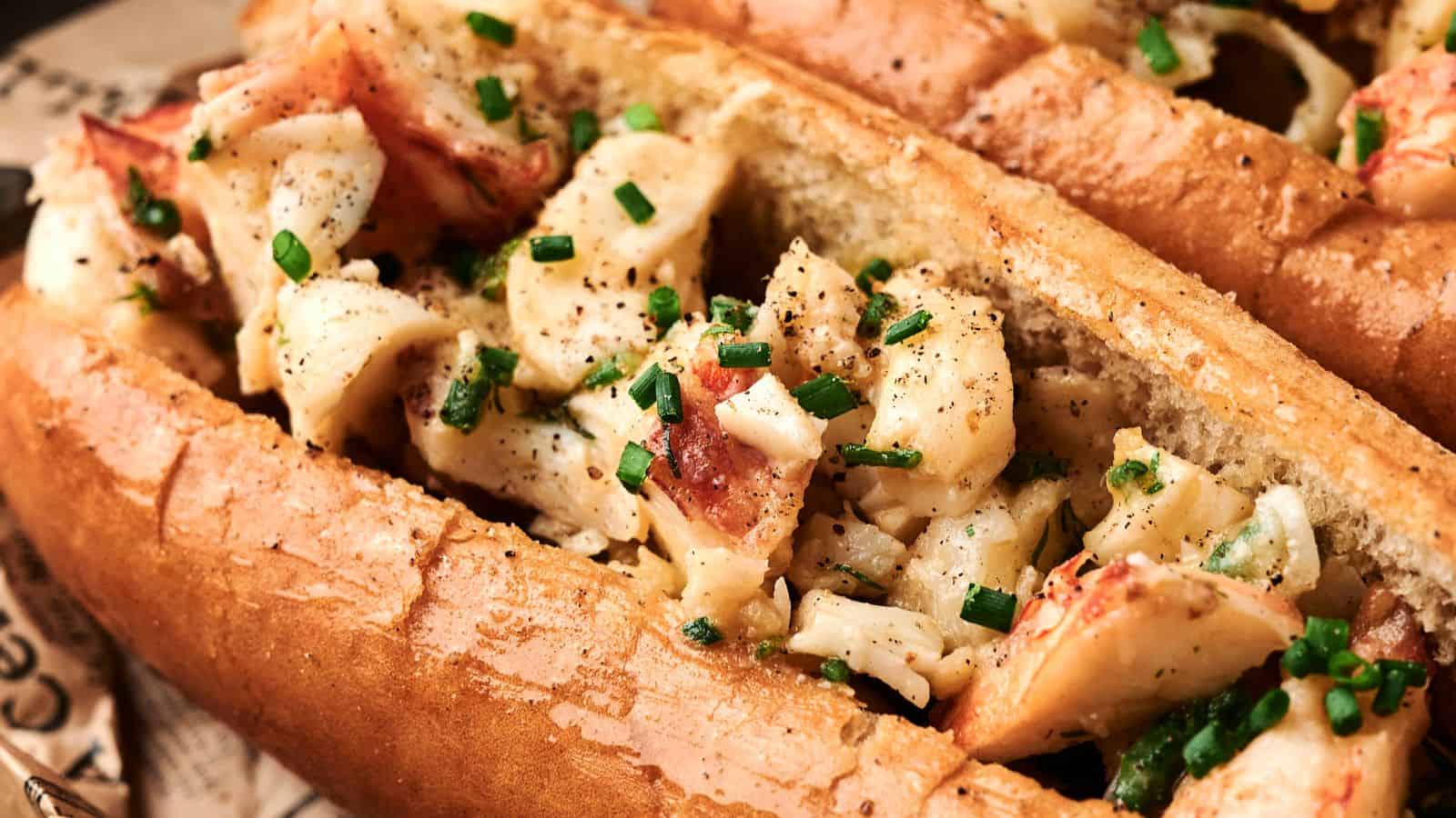 A close-up of a lobster roll topped with chopped chives and black pepper, served in a toasted bun.