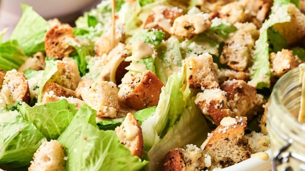 Close-up of a Caesar salad with romaine lettuce, croutons, grated Parmesan cheese, and dressing.