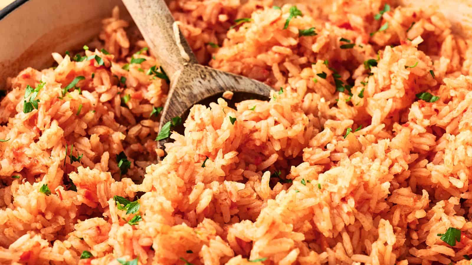 A close-up of cooked Mexican rice with a wooden spoon, garnished with chopped parsley.