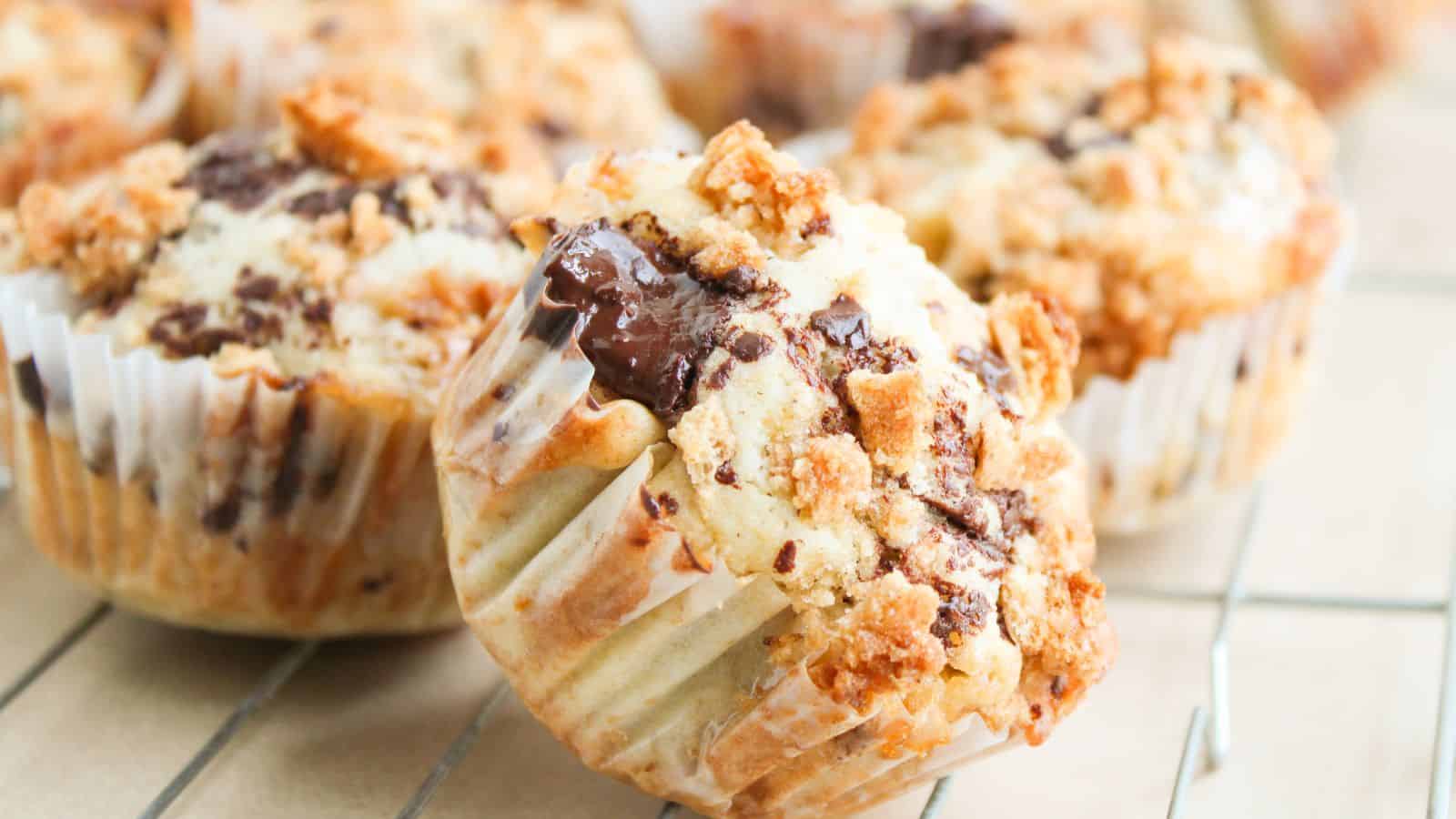 Close-up of chocolate chip muffins with crumb topping in paper liners, cooling on a wire rack.