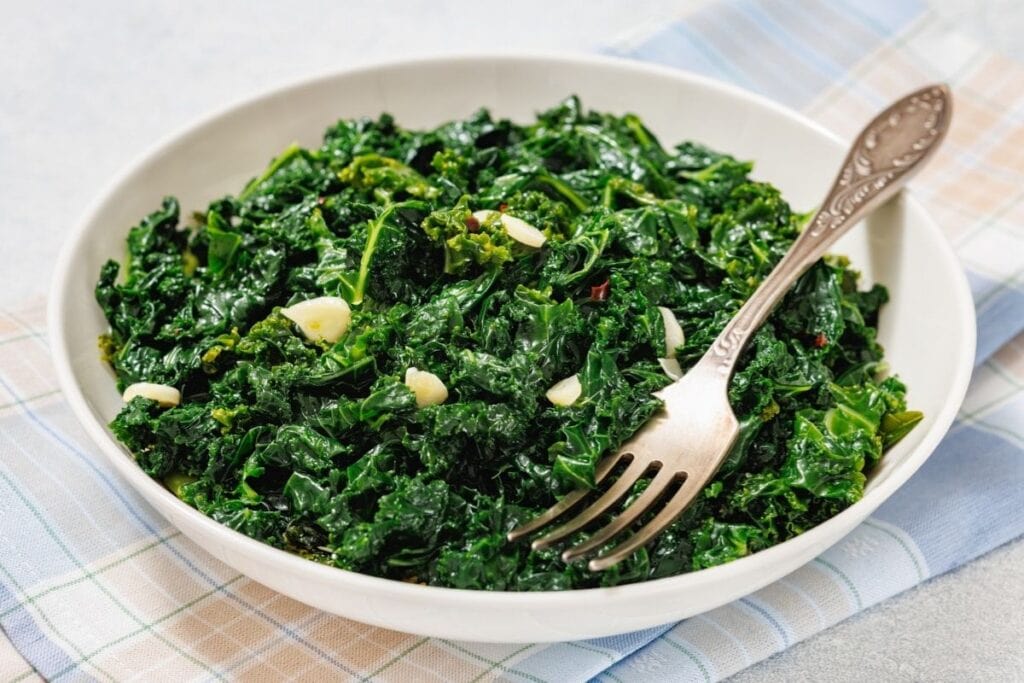 A white bowl filled with Simple Sautéed Kale, with a fork resting on the side.