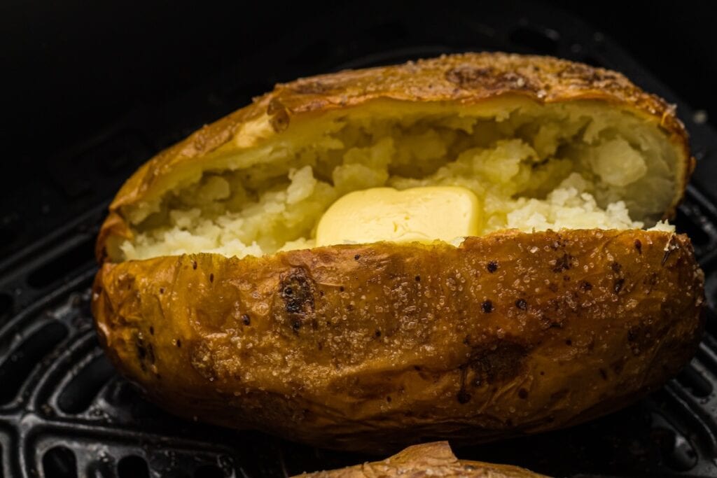 A baked potato with crispy skin is split open, revealing a pat of melting butter inside.