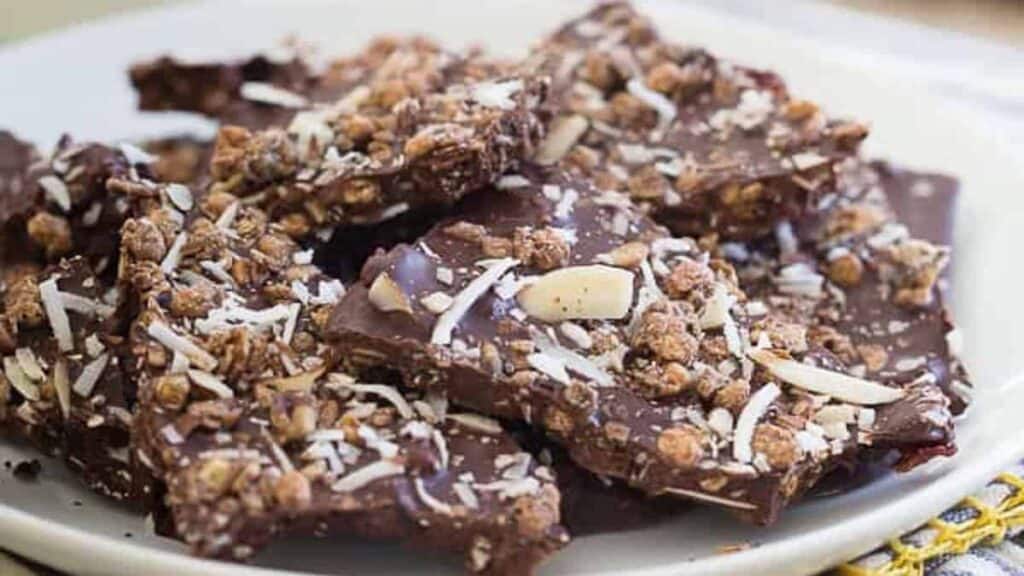 A plate of chocolate bark topped with granola, sliced almonds, and shredded coconut.