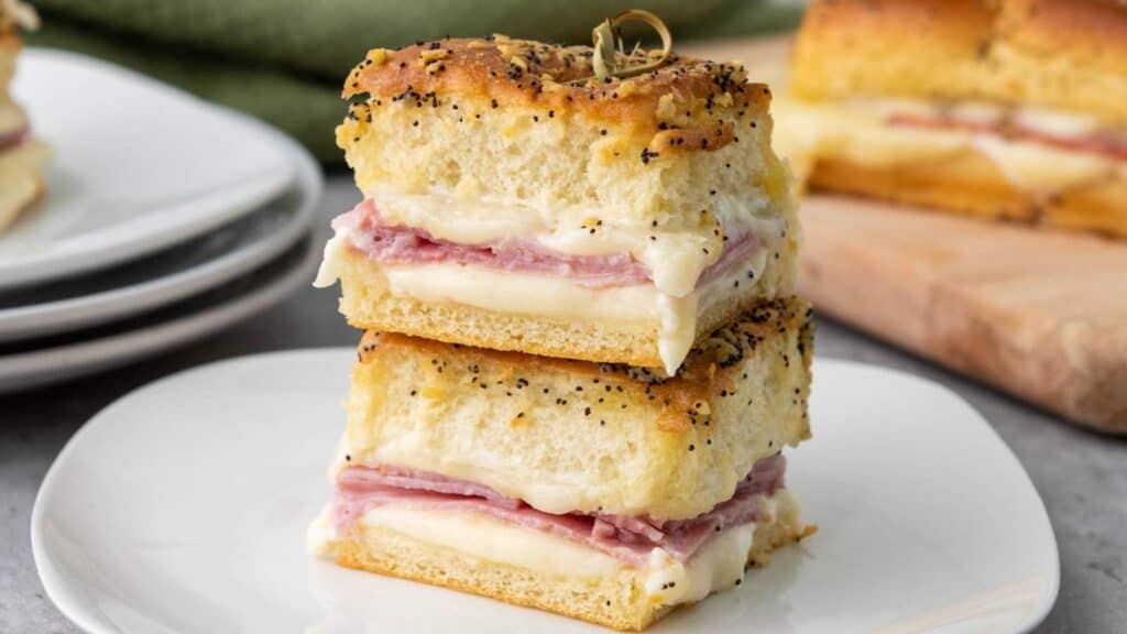 Two stacked sandwiches with layers of ham and melted cheese between thick slices of seasoned bread, served on a white plate.