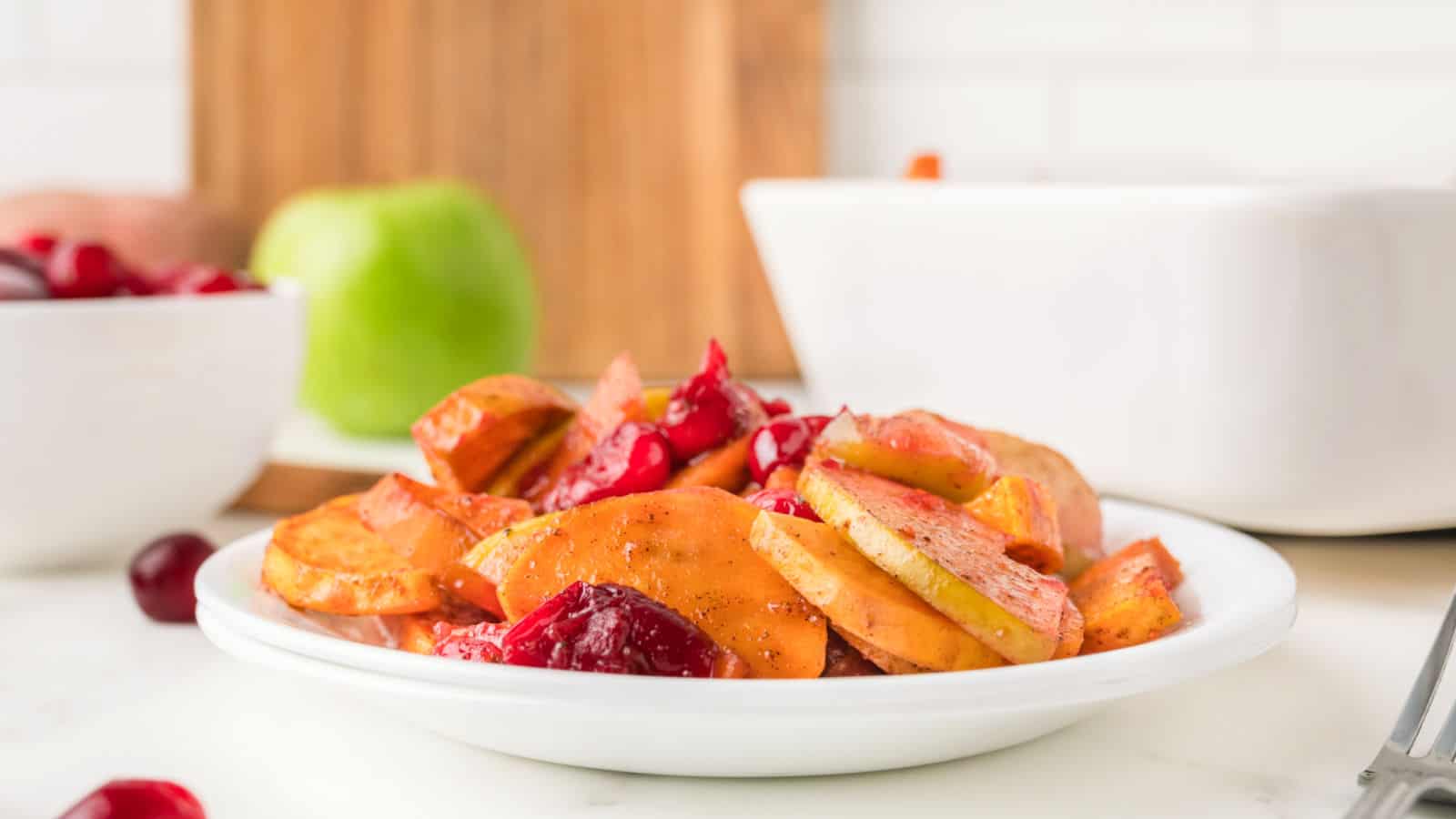 A spoonful of sweet potato slices with apples and cranberries in a white dish.