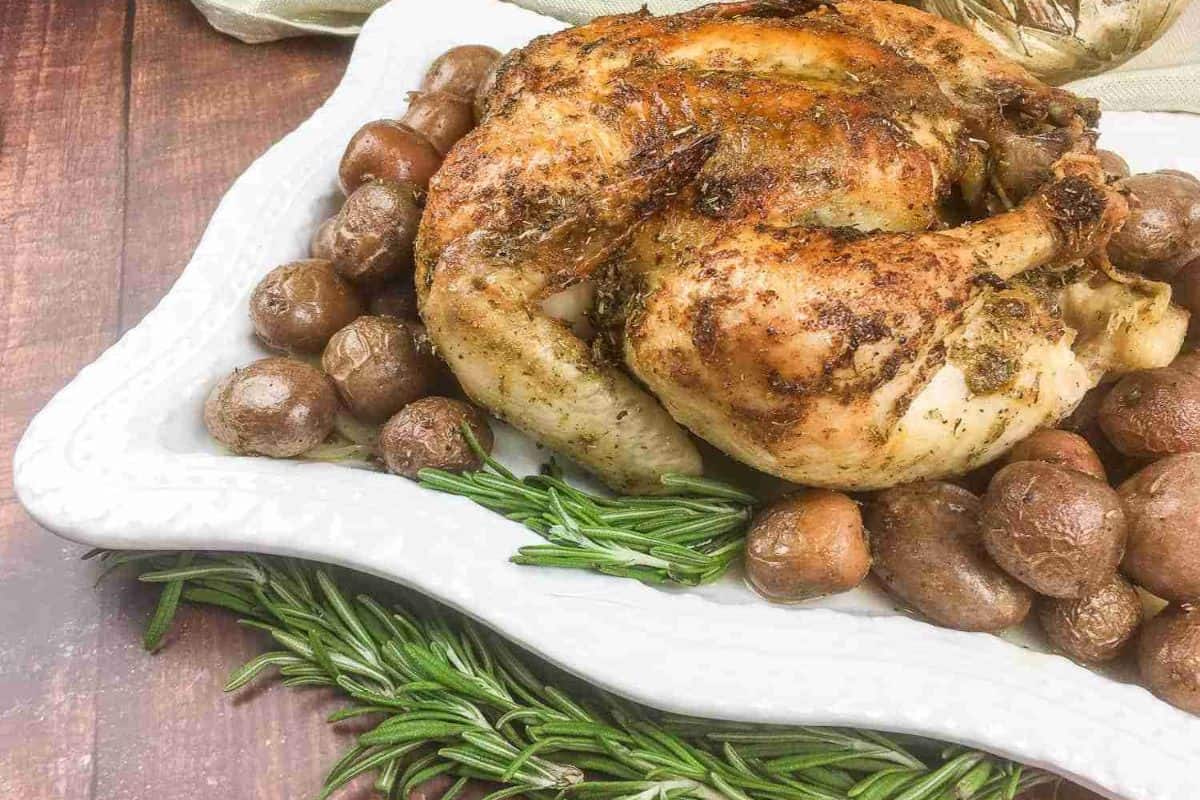Roasted chicken on a white plate, surrounded by roasted potatoes and garnished with fresh rosemary sprigs.